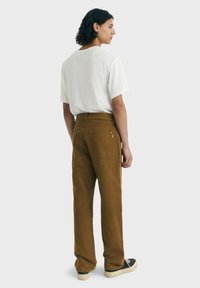 Pantalons en coton marron avec une coupe droite, dotés de poches arrière et de quincaillerie en argent, associés à un t-shirt blanc ample.