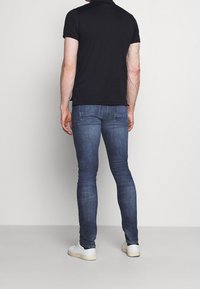 Tmavě modré džíny z denimu s úzkým střihem, zdobené jemným prošitím a dvěma zadními kapsami, v kombinaci s černým polo tričkem a bílými teniskami.