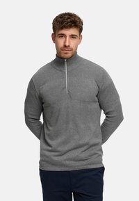 Grå genser med glidelås i halsen og strukturstrikk, med horisontale striper og høy krage. Mykt stoff, lange ermer og tettsittende design.