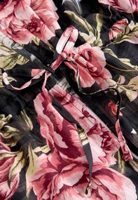 Blommigt tyg med stora rosa och cremefärgade blommor på svart bakgrund, med knutna detaljer och genomskinlig textur.