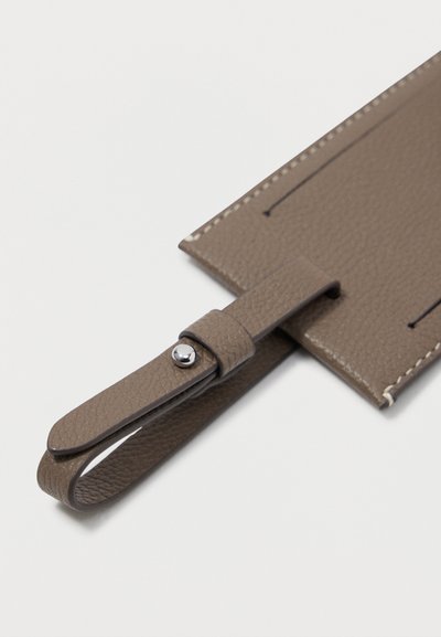 Καφέ δερμάτινη ετικέτα αποσκευών με υφή, ενισχυμένες ραφές και λουράκι προσαρμογής με κούμπωμα από ασημί υλικό.