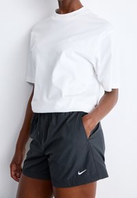 Maglietta bianca in cotone con maniche corte e logo ricamato, abbinata a pantaloncini grigio scuro, leggeri, con vita elastica e un piccolo logo.