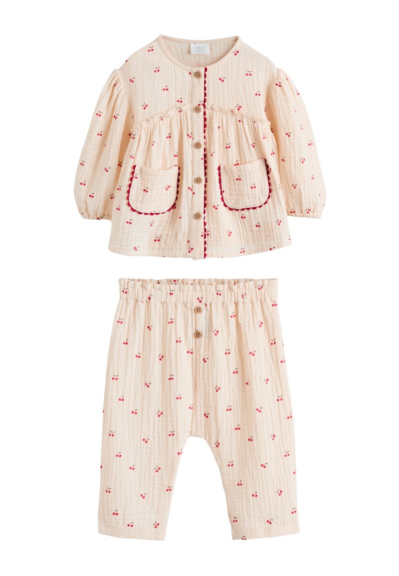 Ensemble deux pièces couleur pêche clair comprenant un haut boutonné à imprimé cerises et manches bouffantes, assorti d'un pantalon à taille élastique. Accents rouges.