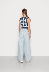 Lyhyt tummansininen ja vaaleansininen ruutukuvioinen neuleen toppi, joka on yhdistetty korkea vyötäröisiin vaaleansinisiin leveisiin farkkuihin ja valkoisiin lenkkareihin.