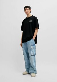 Zwarte katoenen t-shirt met een ronde hals en een klein wit logo, gecombineerd met lichtblauwe cargobroek met meerdere zijzakken en een relaxte pasvorm.