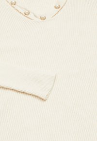 Top crema a coste con scollatura a V, caratterizzato da dettagli perlacei lungo il colletto. Tessuto morbido, forma aderente e maniche lunghe.