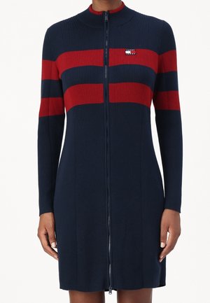 Granatowa sukienka z prążkowanego dzianiny z czerwonymi poziomymi paskami na klatce piersiowej i rękawach, z pełnym przednim suwakiem oraz małą naszywką z logo na lewej stronie klatki piersiowej.