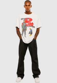 Hvid oversized t-shirt med grafisk design og farverige illustrationer. Parret med mørke jeans og hvide sneakers. Minimale accessories.