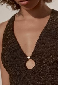 Un tissu noir texturé présente un décolleté en V profond avec une découpe circulaire, reliée par un accent de bague blanche brillante.