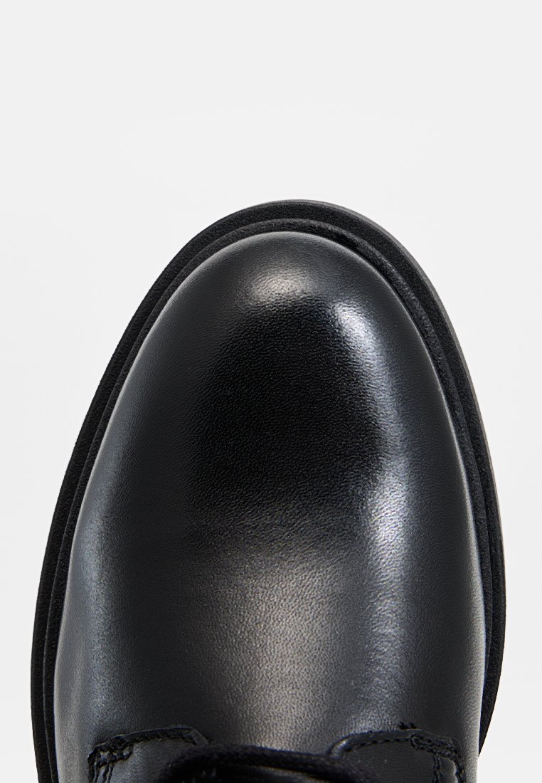 Schwarzer Lederschuh mit einer glatten, glänzenden Spitze, runder Form und strukturierten Akzenten in der Nähe der Schnürsenkel. Flache Gummisohle.