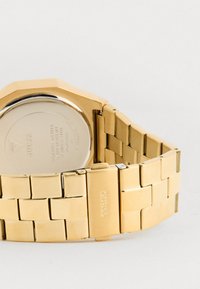 Orologio in acciaio inossidabile dorato con cassa ottagonale, caratterizzato da un bracciale testurizzato e da una chiusura; logo incisi sul link del bracciale.