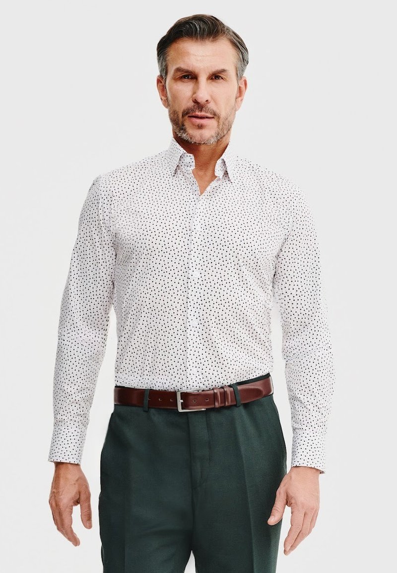 Biała koszula z guzikami, w małe czarne kropeczki, z długim rękawem i zwykłym kołnierzykiem. Połączona z ciemnozielonymi spodniami i brązowym paskiem.