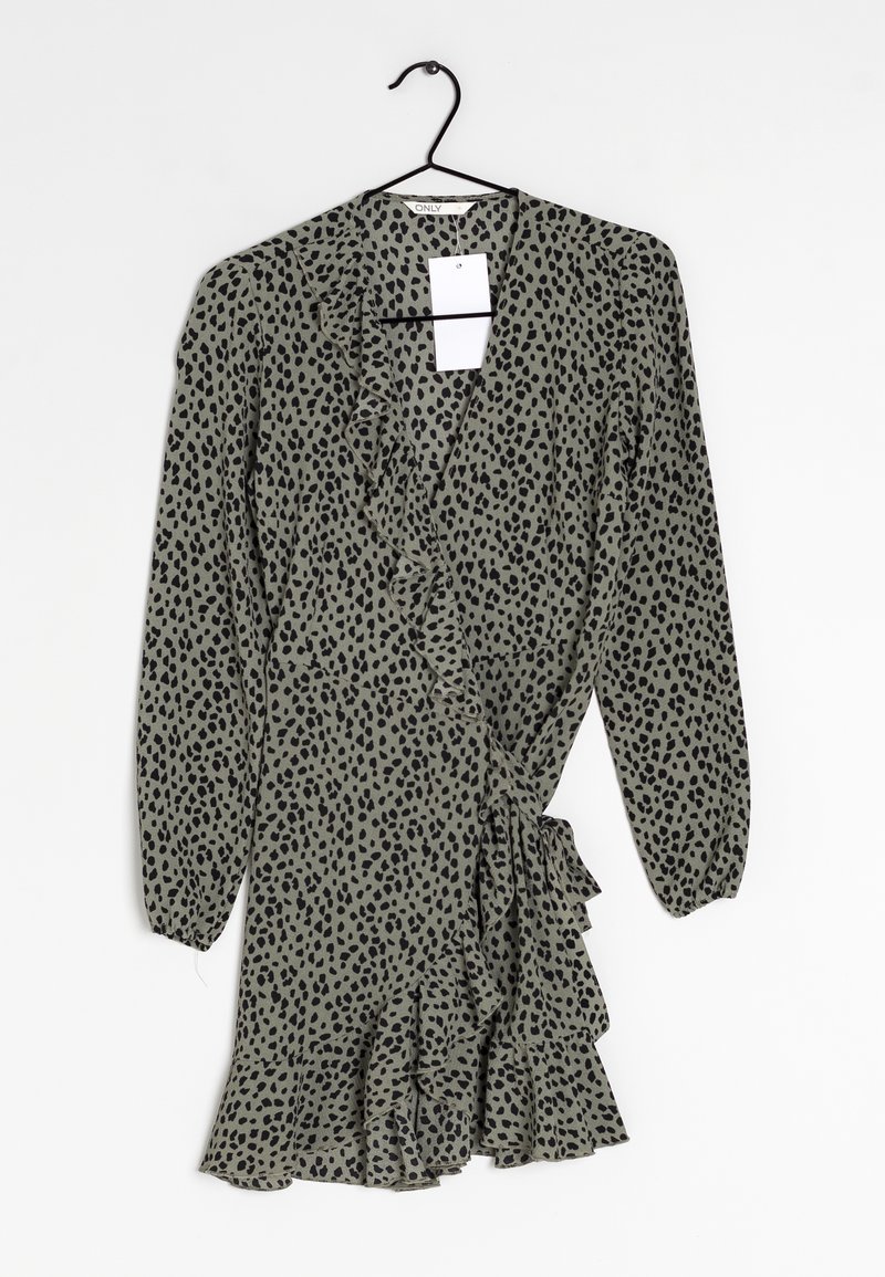 Grünes Kleid mit schwarzem Punktenmuster, Rüsche an der Vorderseite und an den Ärmelbündchen, mittellang, leichter Stoff, hängt an einem schwarzen Haken.