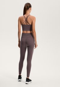 Mauve športová podprsenka s prekríženými popruhmi a legíny so zvýšeným pásom, doplnené čiernymi športovými topánkami. Hladká textura, štýlový dizajn.