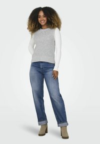 Lichtgrijze geribbelde gebreide tanktop met parelmoeren accenten, gecombineerd met opgerolde blauwe jeans en beige enkellaarsjes.
