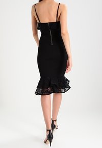 Czarna sukienka bodycon z koronkowym dołem w falbany. Ramiączka spaghetti i zamek z tyłu. Gładka faktura i dopasowany krój.