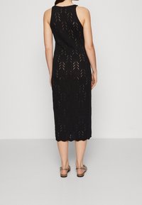 Černé pletené midi šaty s ribbovanou texturou a zigzagovým vzorem, s bezramenným designem a zvlněným lemem.