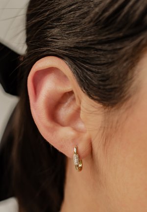 Gouden hoepeloorbellen met een veilige sluiting, met een centrale cluster van kleine, heldere edelstenen. Close-up weergave die het oor benadrukt.