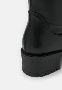 Svart läderankelsko med en kraftig svart gummisula, med synliga sömnadsdetaljer och en snygg, rundad tådesign.