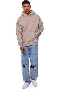 Beige hoodie met een voorzak, gecombineerd met lichtblauwe ripped jeans en witte sneakers. Eenvoudig ontwerp met een relaxte pasvorm.