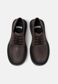 Brune lædersko med gummisål og sorte snørebånd, med "CAMPER" logoet på indersålen, set ovenfra på hvid baggrund.