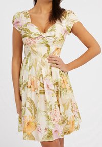El vestido floral presenta una tela de color crema claro con flores rosas y naranjas, un escote corazón, mangas cortas abullonadas y una falda plisada.