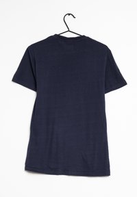 Námořnická modrá bavlněná tričko s kulatým výstřihem a krátkými rukávy, visící na černém háčku na bílém pozadí. Bez vzorů nebo akcentů.