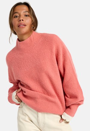 Różowy, oversized sweter z dzianiny z prążkowanym, wysokim kołnierzem i miękką teksturą. Wyróżnia się akcentami na krawędzi w kontrastowym jasnym kolorze.