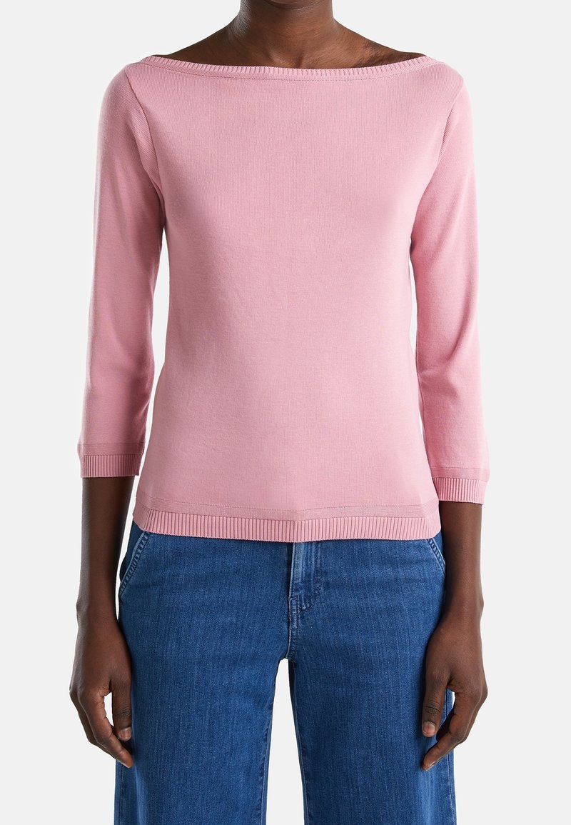 Pink knitted shirt with a wide boat neckline and three-quarter sleeves. Ribbed cuffs and hem, paired with blue wide-leg jeans.