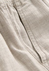 Primer plano de una tela beige texturizada con costuras visibles y detalle de cintura elástica fruncida.
