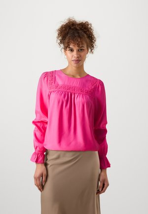 Blouse en satin rose avec un col rond, des détails en dentelle complexe sur la poitrine, et des manches gatherées avec des poignets élastiques.