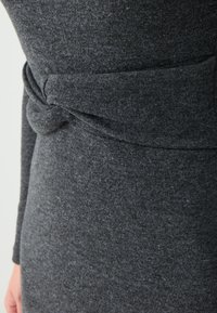 Grau gestrickter Kleidstoff mit weicher Textur. Verfügt über ein verdrehtes Knotendetail an der Taille. Formt eine figurbetonte Silhouette.