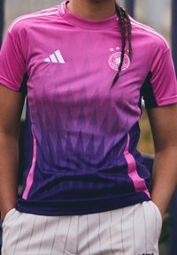 Fioletowo-różowy gradientowy koszulka sportowa z geometrycznymi wzorami, z białym logo Adidas i emblematem na piersi. Krótkie rękawy.