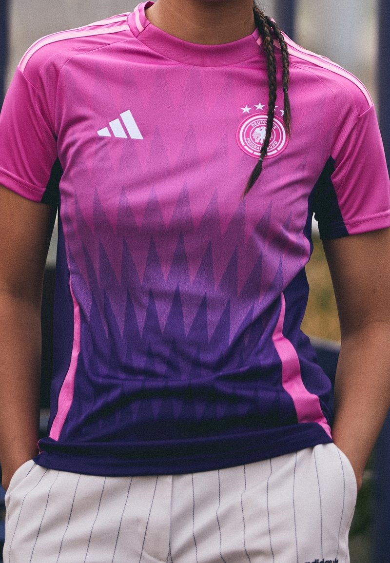 Fioletowo-różowy gradientowy koszulka sportowa z geometrycznymi wzorami, z białym logo Adidas i emblematem na piersi. Krótkie rękawy.