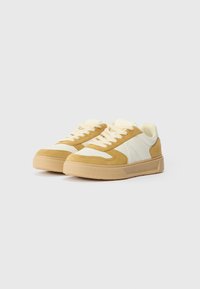 Tan og creme sneakers med en blanding af ruskind og læder, rund tå, tekstureret ydersål og kontrastsnørebånd. Lave sneakers.