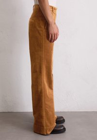 Bruine corduroy broek met een rechte pasvorm, zijzakken en contrasterende stiksels. Gecombineerd met zwarte schoenen.