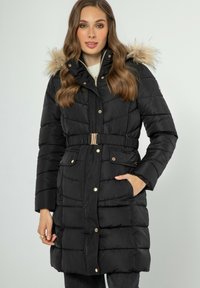 Abrigo de plumas negro con capucha de piel sintética, cintura ceñida, múltiples bolsillos y diseño acolchado. Presenta acentos en tono dorado.