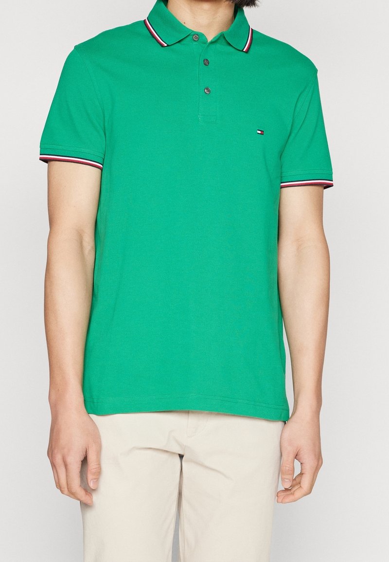 Polo vert avec col, deux boutons et accents contrastants rouge et blanc rayés sur le col et les manches. Matière en coton.
