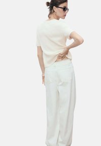 White textured knit short-sleeve top paired with high-waisted white wide-leg jeans. Subtle back slit detail and minimalist design.
