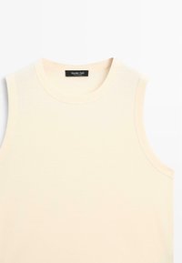 Top senza maniche color beige chiaro realizzato in morbido cotone, con scollatura rotonda e un design semplice senza ulteriori motivi o dettagli.