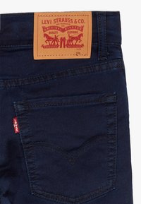 Jeans de mezclilla azul oscuro con una etiqueta de cuero cosida en la cintura, con el logo rojo de Levi's y un diseño distintivo en el bolsillo trasero.