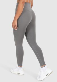 Leggings grigi alti in vita con una texture liscia, caratterizzati da cuciture piatte e un design aderente, abbinati a scarpe da ginnastica bianche.