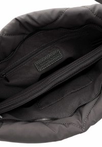 Interior de bolso acolchado negro con una textura suave. Incluye bolsillos con cremallera y una etiqueta de cuero de marca.