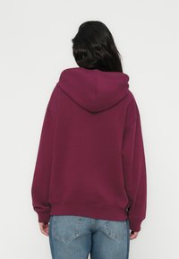 Sweat à capuche bordeaux à coupe ample, avec poignets et ourlet côtelés. Porté avec un jean taille haute bleu clair, affichant un design simple et décontracté.