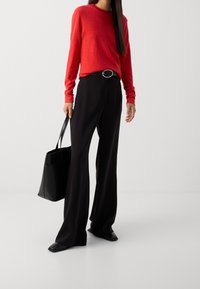 Maglione rosso a maniche lunghe, pantaloni neri a vita alta, scarpe con punta quadrata e borsa tote nera rettangolare. Silhouette bilanciata con toni neutri.