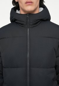 Geacă puffer neagră, quilted, cu guler ridicat și închidere cu fermoar. Dispune de o căptușeală interioară moale și un design minimalist.