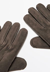 Braune Wildlederhandschuhe mit Fünf-Finger-Design, ausgestattet mit tonal abgesteppten Nähten und einer weichen Textur. Die Handflächen sind schlicht gehalten und sorgen für eine glatte Oberfläche.