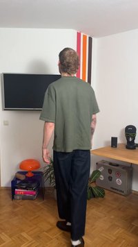 Πράσινο ριγωτό κοντομάνικο πουκάμισο, άνετη γραμμή, σε συνδυασμό με σκούρο τζιν, φορεμένο με καφέ παντόφλες. Στο φόντο φαίνονται τηλεόραση, λάμπα και ράφι.