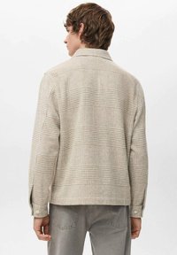 Chaqueta de cuadros beige con tela texturizada, con cuello clásico y puños abotonados, vista desde atrás.