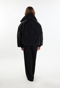Giacca a vento nera con collo alto, motivo a rombi e vestibilità comoda, abbinata a pantaloni neri larghi.